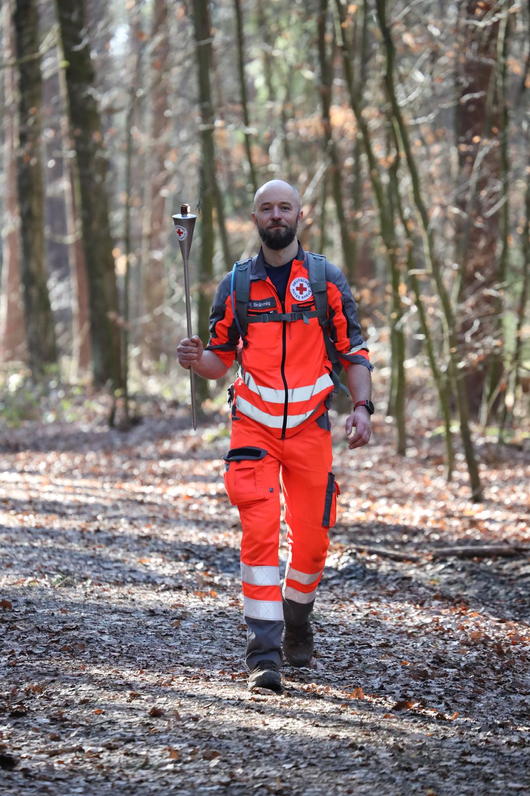 Eine Person in DRK-Uniform laut mit Fackel in der Hand auf einem Waldweg