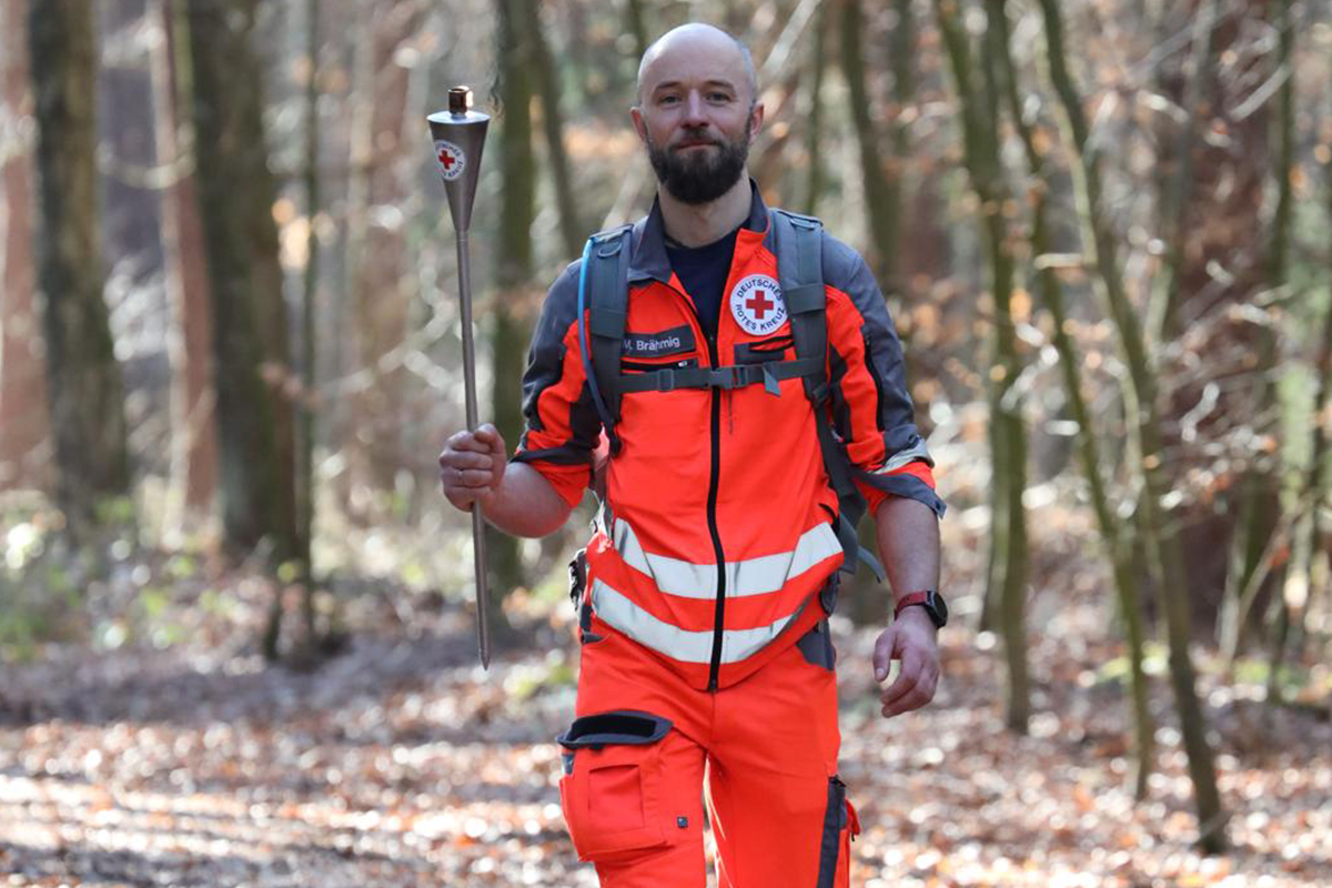 Eine Person in DRK-Uniform laut mit Fackel in der Hand auf einem Waldweg