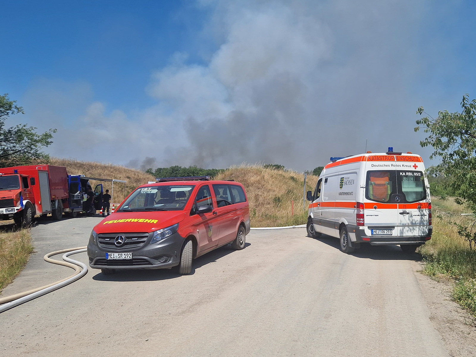 DRK-KTW und Feuerwehrfahrzeuge, im Hintergrund Rauchwolken