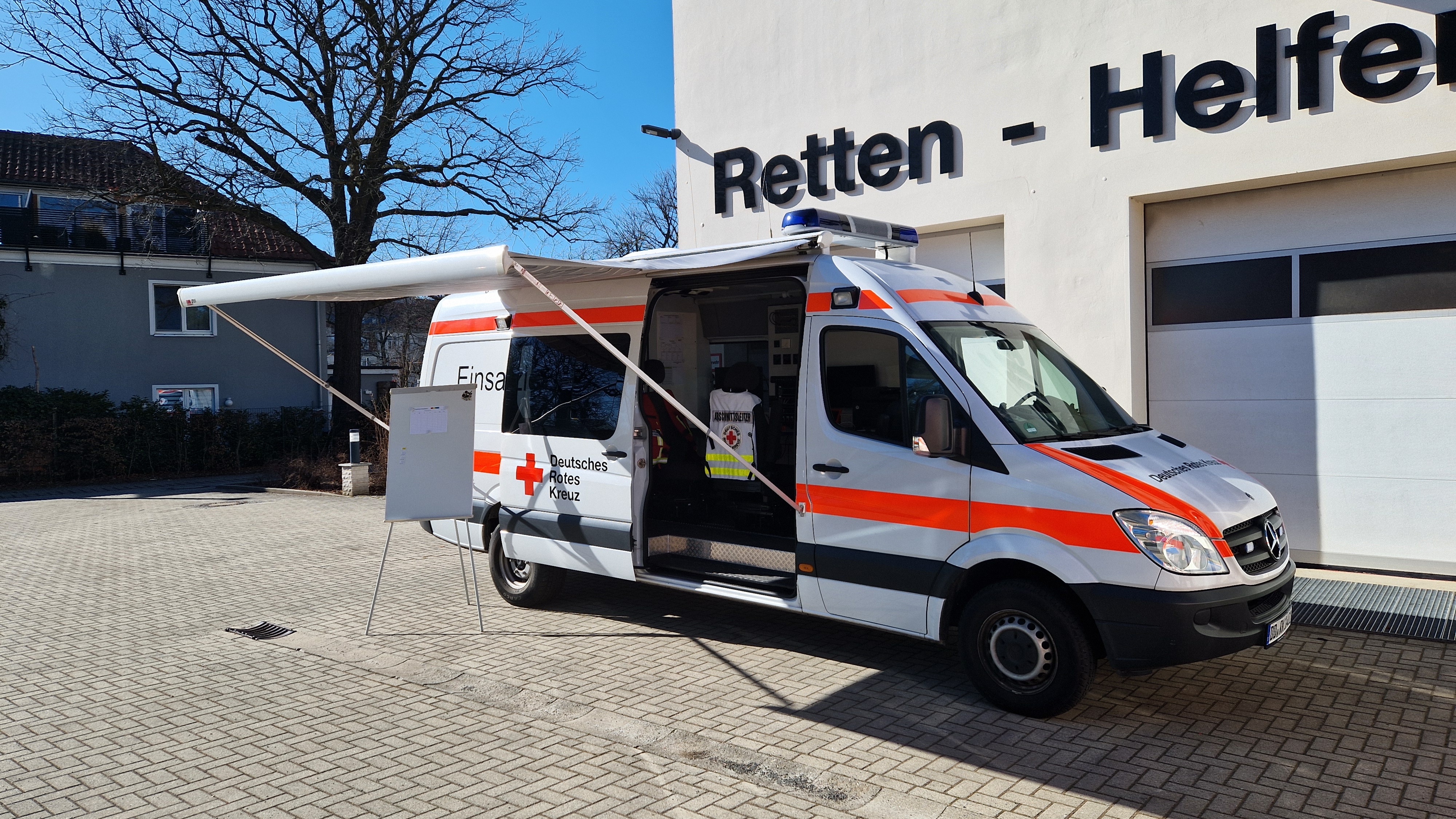 Einsatzleitwagen von außen mit ausgefahrener Markise, im Hintergrund blauer Himmel und eine Halle