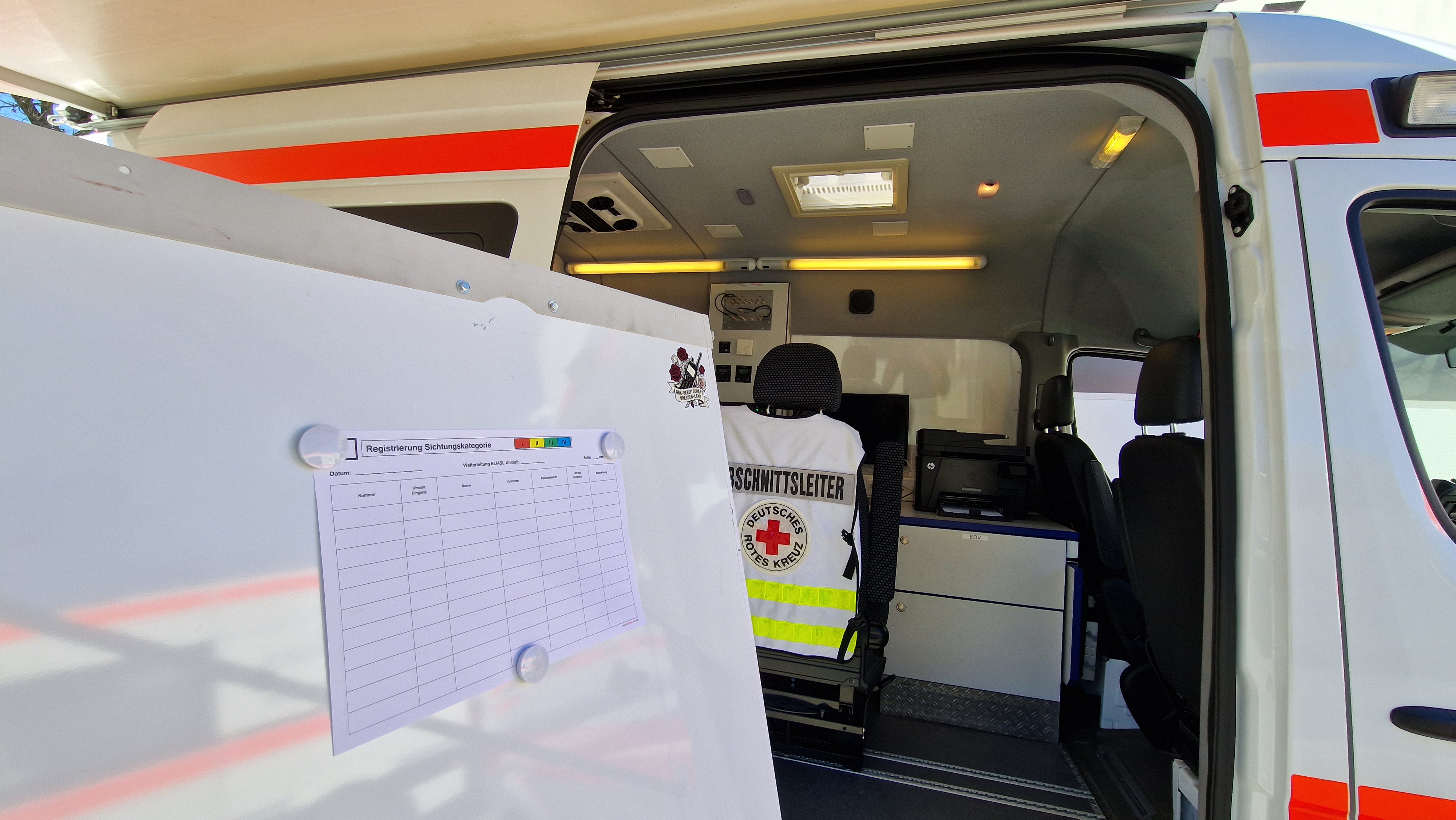 Ein Whiteboard vor der offenen Seitentür eines Fahrzeuges, innen ein Sitz mit weißer Weste