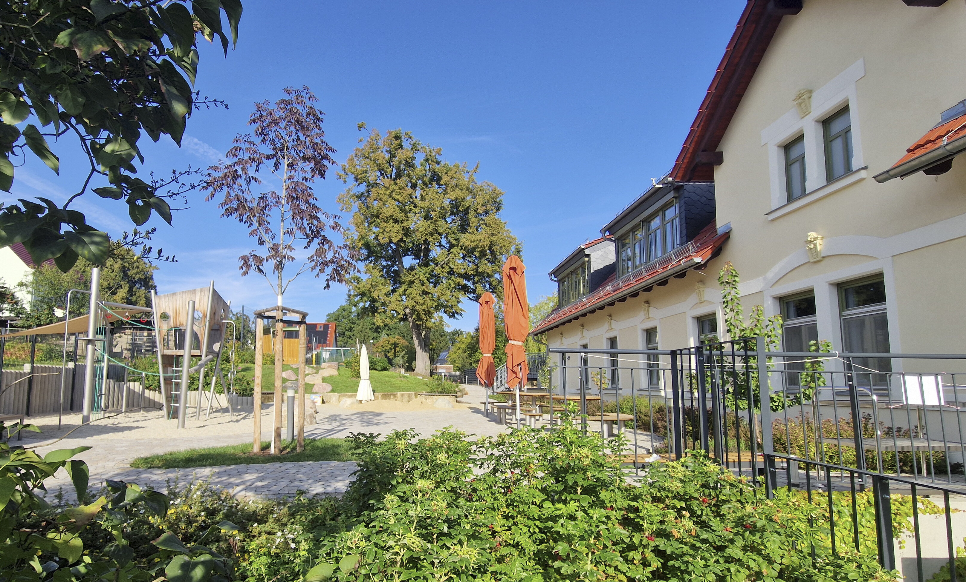Außengelände mit grünen Büschen, blauem Himmel, Klettergerüst