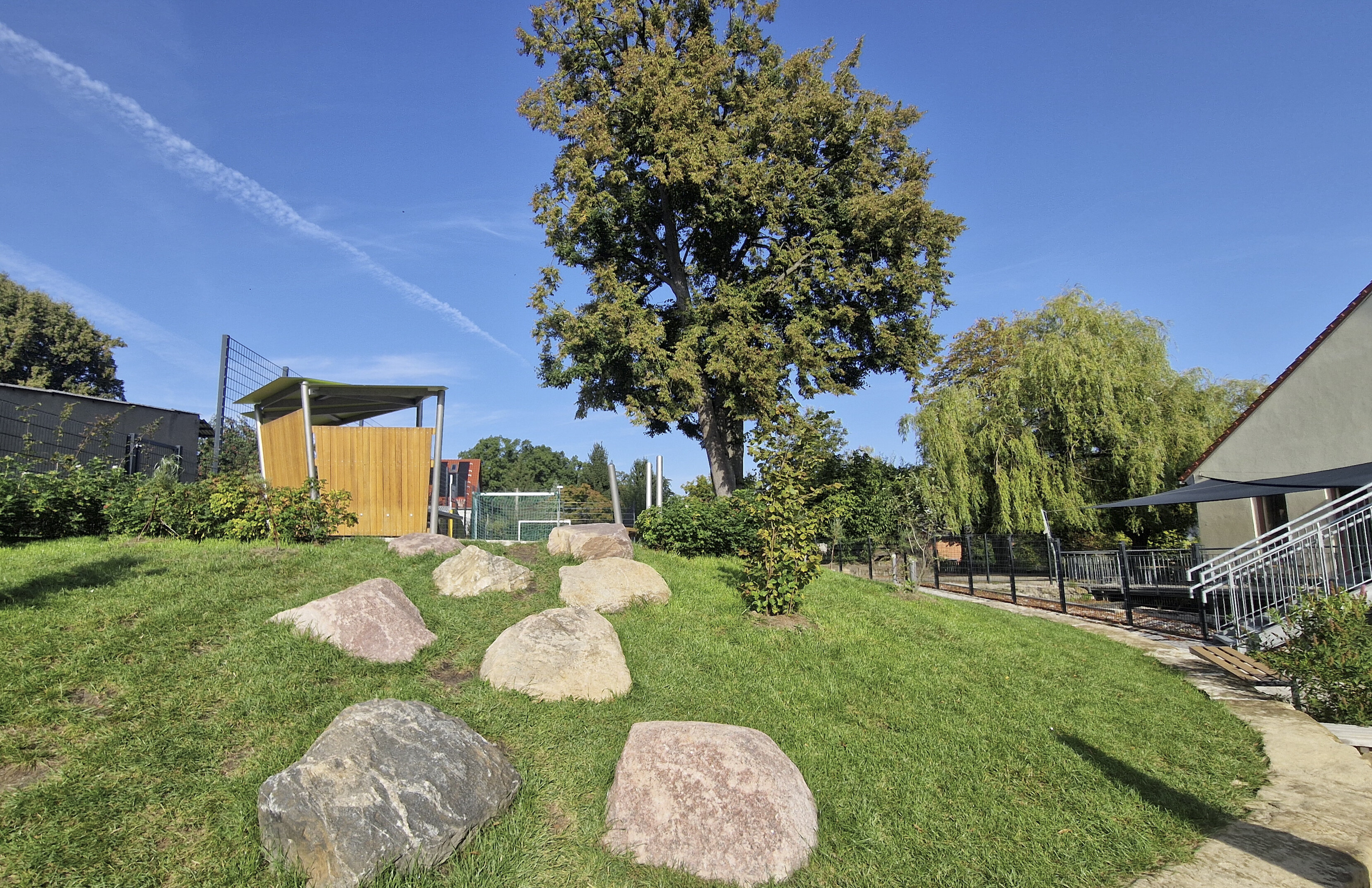 Hügel mit Wiese, großen Steinen und Weg zum Sportplatz