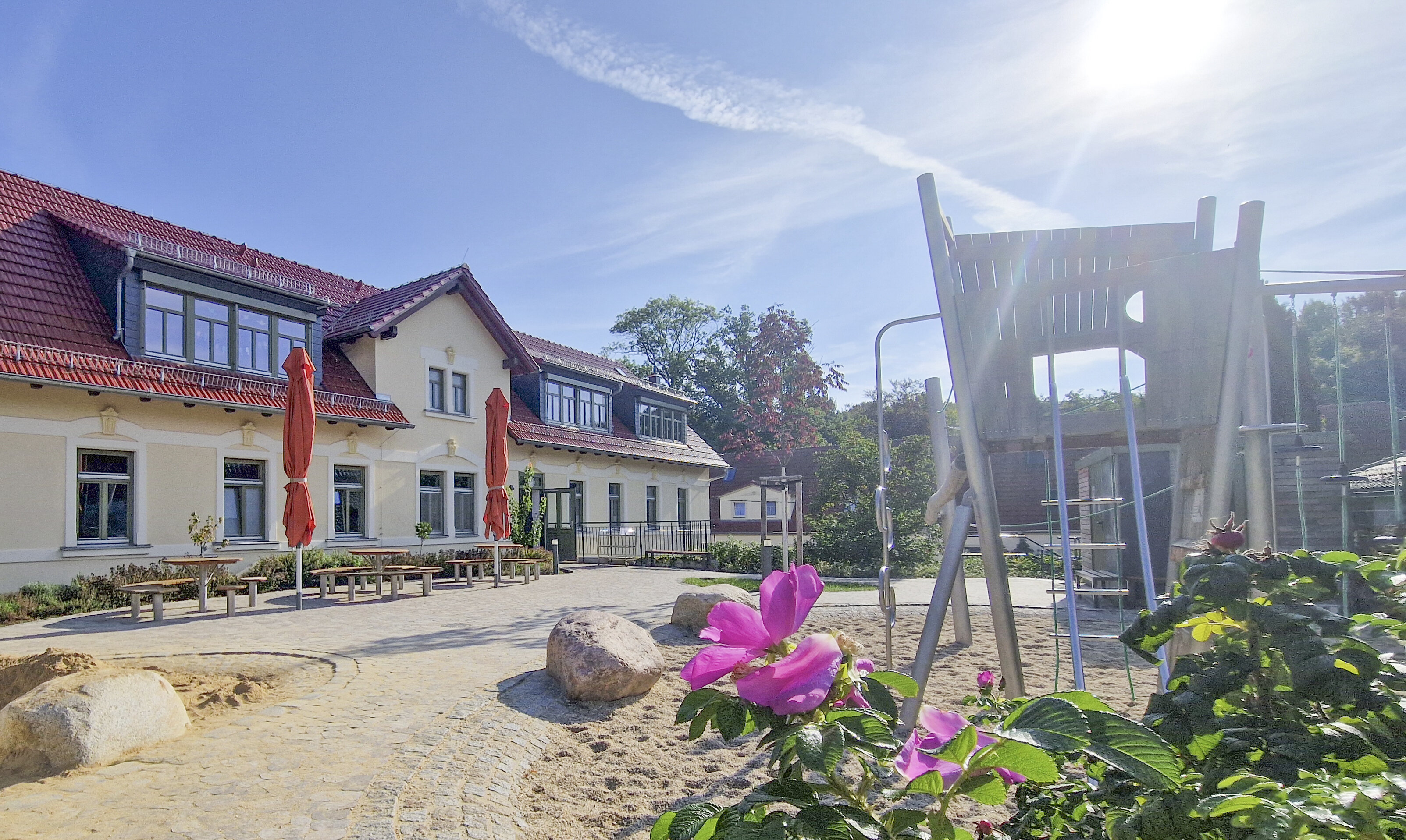 Altes Rittergut-Gebäude, davor gepflasterter Platz, Klettergerüst, pink-farbene Blume