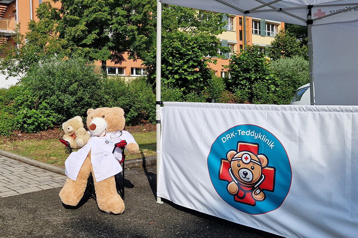 Teddybär in Arztkittel vor Banner "Teddyklinik"
