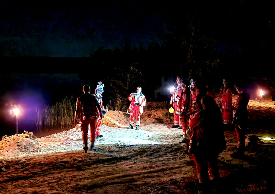 DRK-Einsatzkräfte bei nächtlicher Orientierungsübung, Fackeln und See im Hintergrund