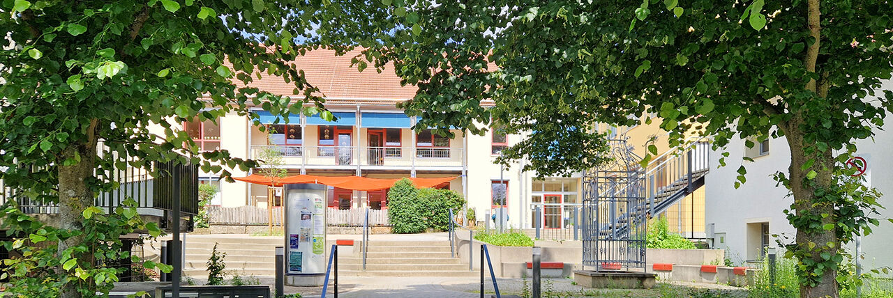 Gebäudefront der DRK-Kita Liegau, im Vordergrund große Laubbäume