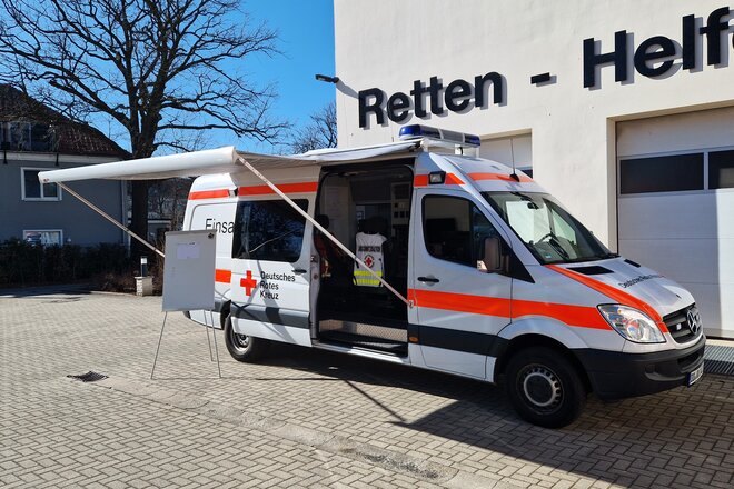 Einsatzleitwagen von außen mit ausgefahrener Markise, im Hintergrund blauer Himmel und eine Halle