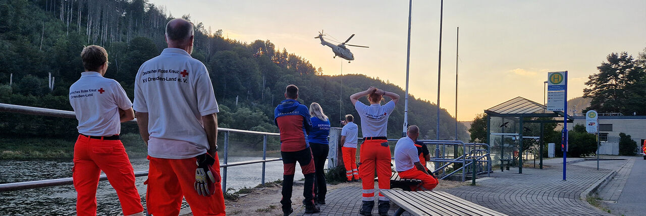 Einsatzkräfte der Bereitschaft betrachten einen Hubschrauber bei der Wasseraufnahme während eines Waldbrandes